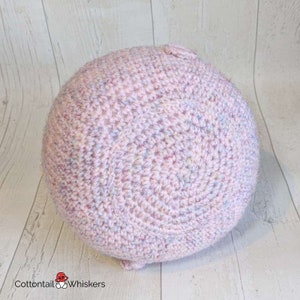 Op de afbeelding: Een roze gehaakte bal met een textuur. De bal is gemaakt met verschillende tinten roze en blauw garen.