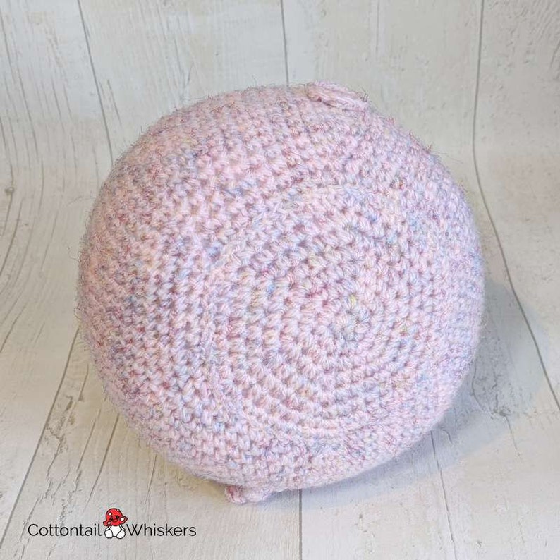 Op de afbeelding: Een roze gehaakte bal met een textuur. De bal is gemaakt met verschillende tinten roze en blauw garen.