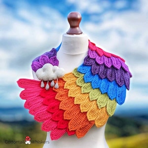 May include: A rainbow crochet collar with a cloud and raindrops charm. The collar is made of crocheted scales in a rainbow pattern, with a white cloud charm with silver raindrops hanging from it.