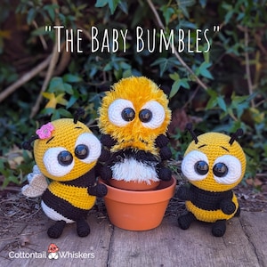 May include: Three handmade crochet bee dolls. The bees are yellow and black, with large white eyes. One bee has a pink flower on its head and wings. The text "THE BABY BUMBLES" is above the bees. The logo "Cottontail Whiskers" is at the bottom.