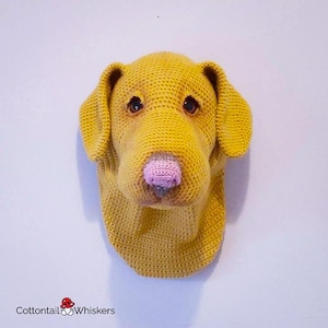May include: A crocheted dog head wall hanging in a yellow color with a pink nose.