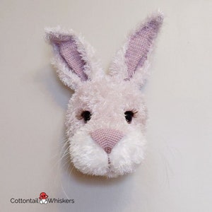 May include: A crocheted bunny rabbit head with pink ears and a white fluffy face. The bunny has black eyes and a pink nose.