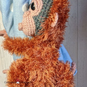 May include: A crocheted orangutan plush toy with a brown and orange fur. The toy has a pink face with black eyes and a green and brown hat.