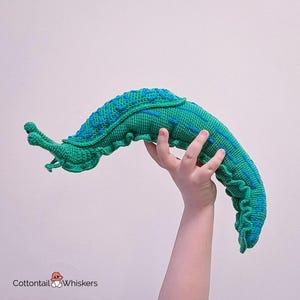 K&ouml;nnte beinhalten: Ein geh&auml;keltes gr&uuml;nes und blaues Pl&uuml;schtier in Form einer Schnecke. Die Schnecke ist zu einem C gekr&uuml;mmt und hat eine strukturierte Oberfl&auml;che.