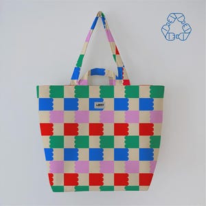 May include: A beige tote bag with a colorful checkerboard pattern of red, green, blue, and pink shapes. The bag has matching handles and a small label that reads "LORE". A recycling symbol is in the upper right corner.