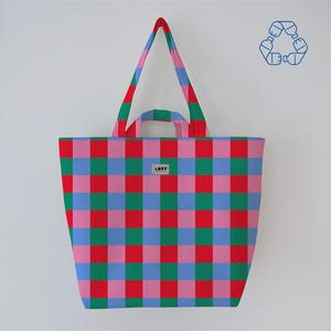 May include: A large tote bag with a colorful checkered pattern in red, pink, green, and blue. The bag has long handles and a small silver tag that reads "LORE". A recycling symbol is in the upper right corner.