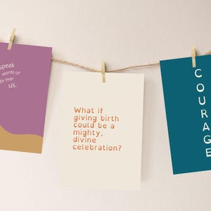 Puede incluir: Tres tarjetas rectangulares cuelgan de una cuerda con pinzas de madera. Las tarjetas son moradas, crema y verde azulado. La tarjeta morada tiene el texto "Hablo palabras de vida sobre nosotros". La tarjeta crema dice "¿Y si dar a luz pudiera ser una celebración poderosa y divina?" La tarjeta verde azulado dice "CORAJE."