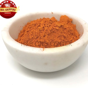 May include: A small white bowl filled with a bright orange powder. The powder is finely ground and has a smooth texture.