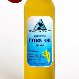 May include: A clear glass bottle of organic virgin corn oil with a blue and white label. The label says "Health & Beauty", "Organic Virgin Corn Oil", "Zea Mays", "Pure and Natural", "Extraction Method: Cold Pressed Unrefined", "Obtained from SEEDS", "Country of Origin Spain", and "Exp. date". The bottle is 12 fluid ounces (355 ml).