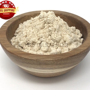 May include: A close-up of a wooden bowl filled with a light beige powder. The powder is smooth and evenly distributed throughout the bowl.