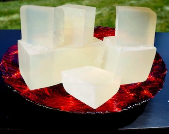 May include: A group of clear, rectangular soap bars arranged on a red and white swirl patterned plate. The soap bars are stacked on top of each other and are arranged in a pyramid shape.