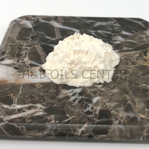 May include: A close-up of a white powder on a brown marble surface. The powder is in a small pile and is slightly rounded. The text "H&B OILS CENTER" is visible on the surface.