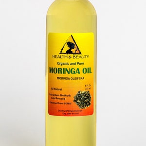 May include: A clear glass bottle with a yellow label containing 8 fluid ounces of organic and pure Moringa Oil. The label features a triangle with a woman's silhouette inside, the words "Health & Beauty", and the text "Moringa Oil Moringa Oleifera". The label also states that the oil is all natural, cold pressed, obtained from seeds, and made in Denmark.