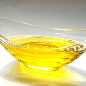 Puede incluir: Un bol de vidrio transparente lleno de un l&iacute;quido amarillo brillante, probablemente aceite, con un ligero efecto de ondulaci&oacute;n en la superficie.