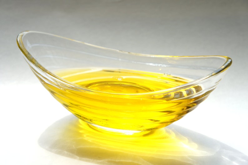 Puede incluir: Un bol de vidrio transparente lleno de un l&iacute;quido amarillo brillante, probablemente aceite, con un ligero efecto de ondulaci&oacute;n en la superficie.