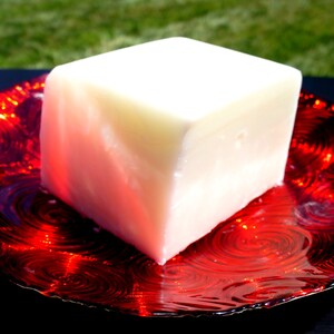 Puede incluir: Un bloque de jab&oacute;n blanco de forma cuadrada sobre un plato rojo con un patr&oacute;n de espiral.
