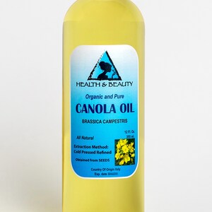 May include: A clear glass bottle of organic and pure canola oil, labeled "HEALTH & BEAUTY CANOLA OIL BRASSICA CAMPESTRIS", with a yellow flower graphic and the text "All Natural 12 Fl. Oz 355 ml Extraction Method: Cold Pressed Refined Obtained from SEEDS Country Of Origin Italy Exp. date"