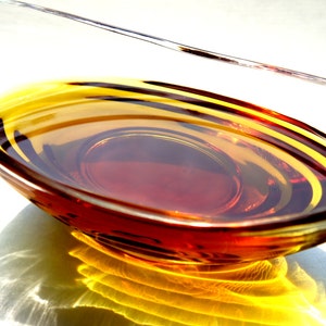 May include: A clear glass bowl filled with a golden brown liquid, creating concentric circles of light and dark shades.