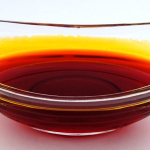 May include: A clear glass bowl filled with a red-orange liquid. The liquid has a thin layer of yellow oil on top.