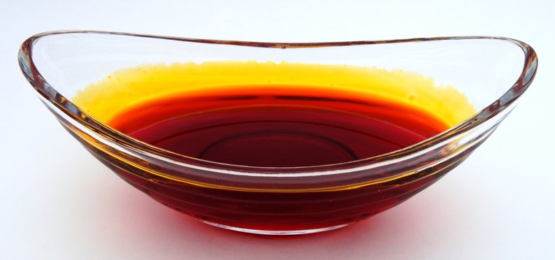 May include: A clear glass bowl filled with a red-orange liquid. The liquid has a thin layer of yellow oil on top.