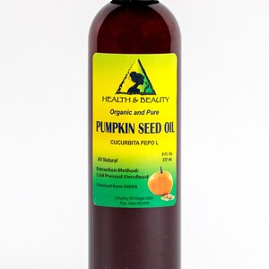 May include: A brown glass bottle with a black cap containing 8 fluid ounces (237 ml) of organic and pure pumpkin seed oil. The label is yellow with green text and a green triangle containing a silhouette of a woman. The label reads "HEALTH & BEAUTY", "Organic and Pure", "PUMPKIN SEED OIL", "CUCURBITA PEPO L", "All Natural", "Extraction Method: Cold Pressed Unrefined", "Obtained from SEEDS", "Country of Origin USA", "Exp. date". A small image of a pumpkin is on the label.