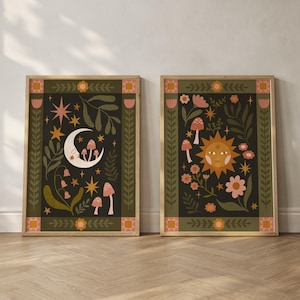May include: Two framed art prints with a celestial theme. One features a crescent moon, mushrooms, and stars. The other showcases a sun, flowers, and mushrooms. Both have a dark background with a decorative border and gold frames.