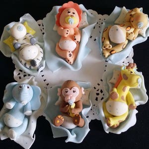 May include: A collection of six baby animal figurines, including a zebra, lion, leopard, elephant, monkey, and giraffe. Each figurine is lying on a light blue blanket with white polka dots. The figurines are made of a smooth, colorful material.
