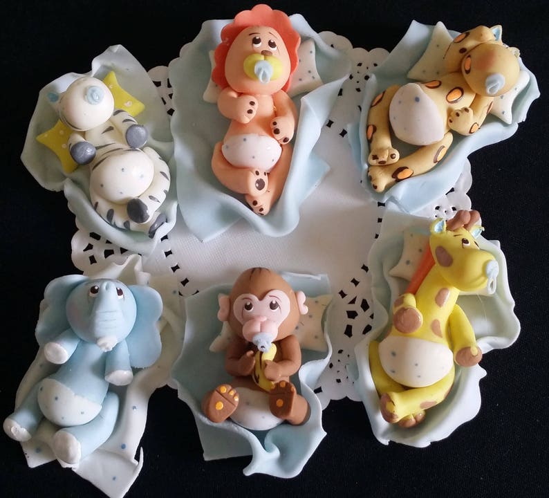 May include: A collection of six baby animal figurines, including a zebra, lion, leopard, elephant, monkey, and giraffe. Each figurine is lying on a light blue blanket with white polka dots. The figurines are made of a smooth, colorful material.