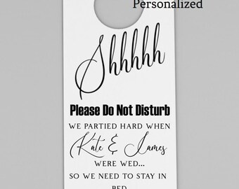 May include: White personalized hotel door hanger, 4.25" x 11", with a circular cutout for the doorknob. The text reads "Shhhhh, Please Do Not Disturb" and includes wedding details. Features a heart symbol.