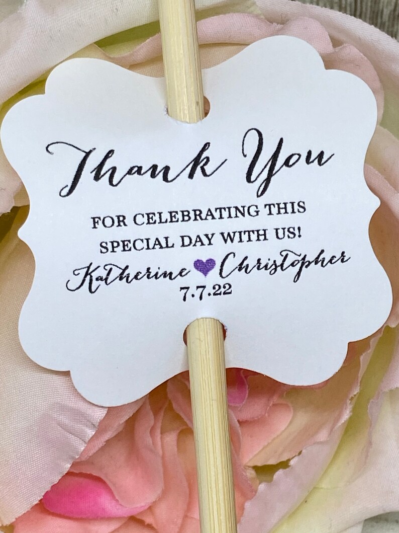 May include: White thank you card with a scalloped edge attached to a wooden stick. The card says "Thank You" and "For celebrating this special day with us! Katherine & Christopher 7.7.22".