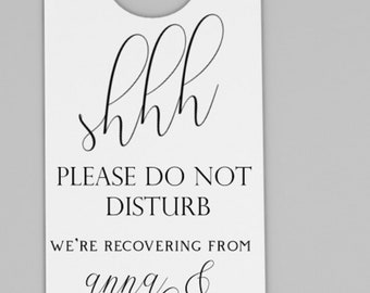 May include: White door hanger with a hole at the top for hanging. The text reads "shh PLEASE DO NOT DISTURB WE'RE RECOVERING FROM anna & stephen's WEDDING".