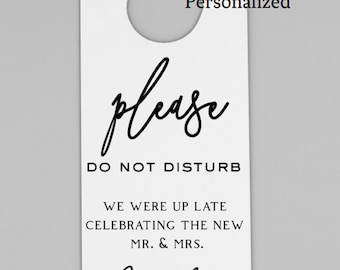 May include: White hotel door hanger with black text that reads "Please Do Not Disturb. We were up late celebrating the new Mr. & Mrs. Davidson". The hanger is 4.25 inches by 11 inches.