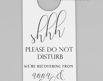 May include: White door hanger with a hole at the top for hanging. The text reads "shhh Please do not disturb We're recovering from anna & stephen's WEDDING".