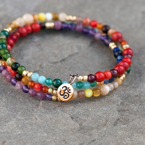 Puede incluir: Pulsera de cuentas multicolores con un dije de Om dorado. La pulsera presenta una variedad de piedras, incluyendo rojo, verde, azul y amarillo.