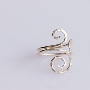 May include: A silver ring with a hammered finish and a swirling design.