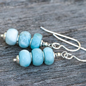 Può includere: Un paio di orecchini d'argento con perline di pietre preziose blu chiaro. Gli orecchini hanno un design semplice e sono perfetti per l'uso quotidiano.