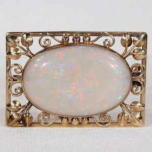 May include: A vintage gold brooch with an oval opal gemstone set in a delicate filigree frame. The frame features a floral design with leaves and swirls.
