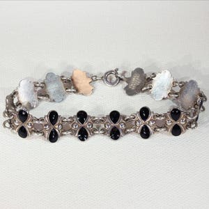 Pu&ograve; includere: Un braccialetto d'argento con accenti in smalto nero. Il braccialetto presenta un design a catena delicato e una chiusura a moschettone.