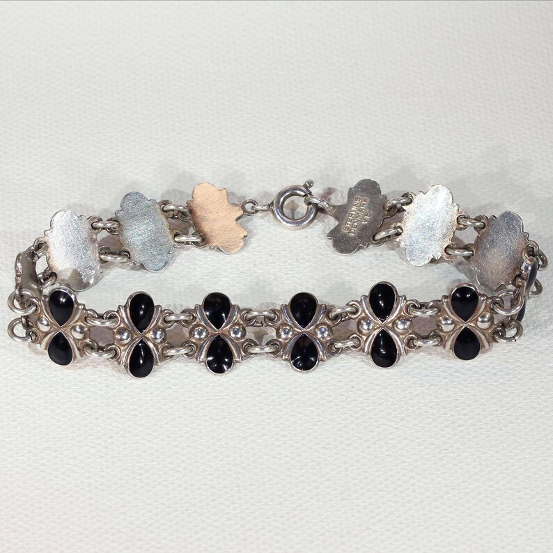 Pu&ograve; includere: Un braccialetto d'argento con accenti in smalto nero. Il braccialetto presenta un design a catena delicato e una chiusura a moschettone.