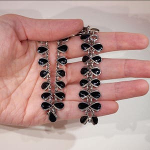 Pu&ograve; includere: Una collana a catena d'argento con pietre nere a forma di goccia. La collana &egrave; realizzata in argento sterling e presenta una catena delicata con pietre di onice nero.
