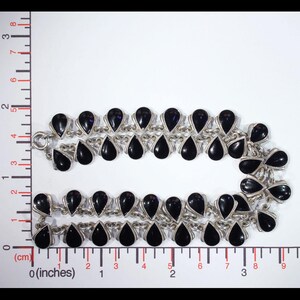 Pu&ograve; includere: Una collana d'argento con pietre nere a forma di goccia. La collana &egrave; a doppio filo e ha una catena delicata.