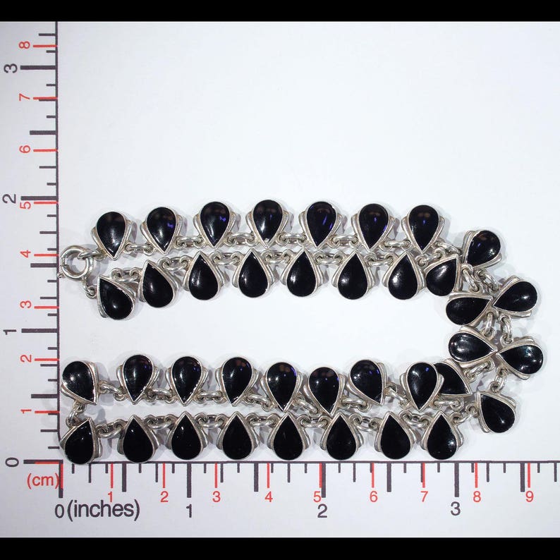 Pu&ograve; includere: Una collana d'argento con pietre nere a forma di goccia. La collana &egrave; a doppio filo e ha una catena delicata.