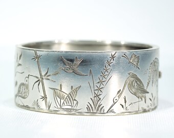 Puede incluir: Un brazalete de plata con un diseño grabado de pájaros, plantas y un barco. El diseño es intrincado y detallado, y el brazalete es un hermoso ejemplo de joyería antigua.