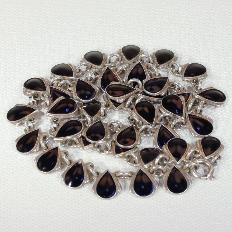 Pu&ograve; includere: Una collana d'argento con pietre nere a forma di goccia. La collana &egrave; realizzata con una catena con un ciondolo a forma di goccia su ogni anello.