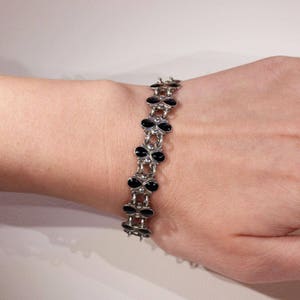 Pu&ograve; includere: Un braccialetto d'argento con ciondoli a forma di trifoglio in smalto nero. Il braccialetto &egrave; al polso.