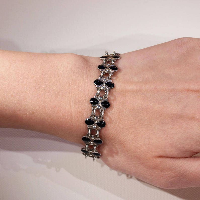 Pu&ograve; includere: Un braccialetto d'argento con ciondoli a forma di trifoglio in smalto nero. Il braccialetto &egrave; al polso.