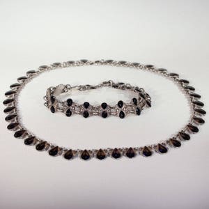 Pu&ograve; includere: Un set di collana e braccialetto in argento con pietre nere a forma di goccia. La collana &egrave; pi&ugrave; lunga e ha una catena pi&ugrave; delicata, mentre il braccialetto &egrave; pi&ugrave; corto e ha una catena pi&ugrave; robusta.