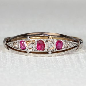 Pode incluir: Um anel de prata e ouro com uma fileira de rubis vermelhos e diamantes engastados em uma banda delicada.