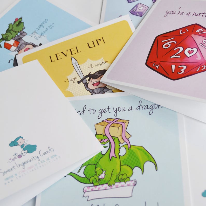 Puede incluir: Un conjunto de tarjetas de felicitaci&oacute;n con varias ilustraciones y texto. Una tarjeta presenta un drag&oacute;n verde con una cinta rosa, otra tarjeta tiene un caballero con una espada y una tercera tarjeta tiene un dado rojo de 20 caras.