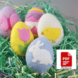 May include: Five felt Easter egg ornaments with different designs. The eggs are in a bed of green and yellow shredded paper. The designs include a butterfly, a tulip, a chick, a bunny, and a striped egg.